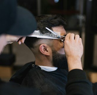 A barber carefully styling a client's hair with a comb.