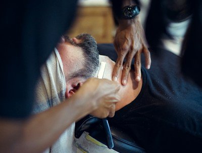 A barber gently shaving a man's beard with a straight razor.