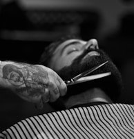 grayscale photography of person holding scissor clipping man's beard